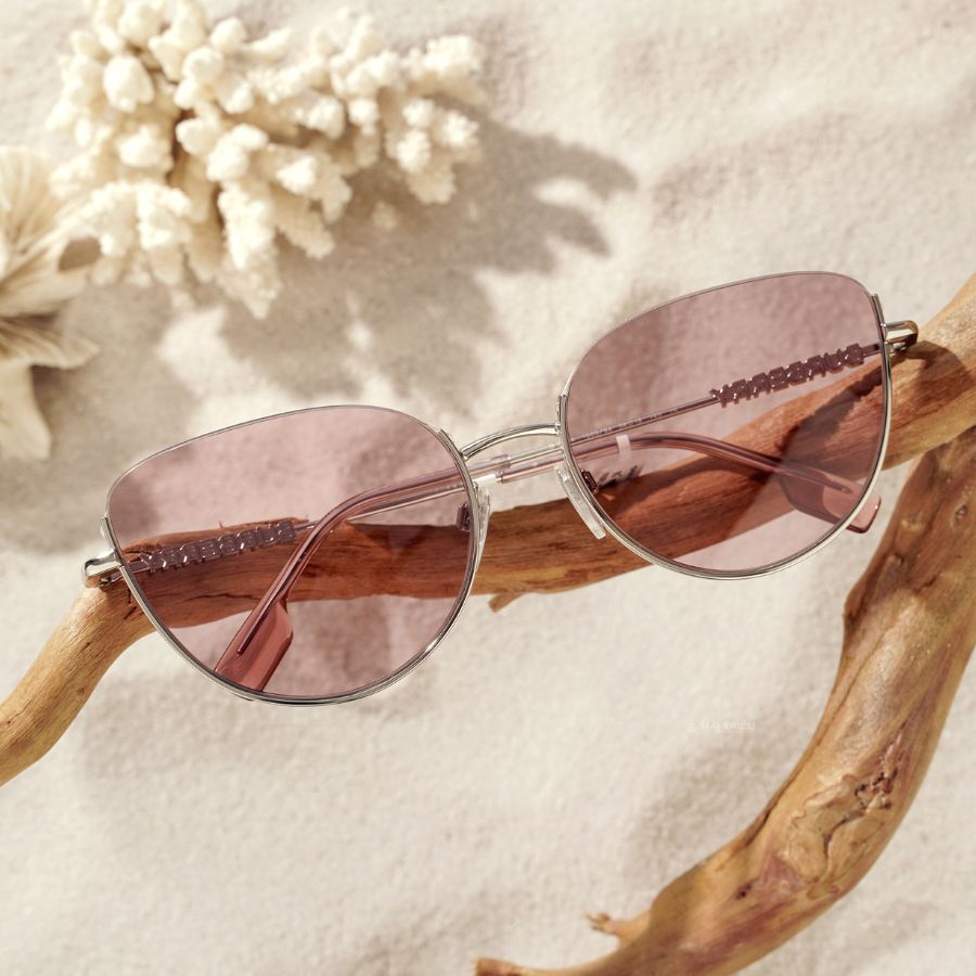 Chiếc kính mát mắt mèo, tròng hồng viền kim loại đang được bày trí trên bãi cát